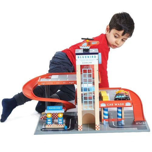 Een jongen in een rood shirt speelt met de Tender Leaf Toys houten garage en servicestation.