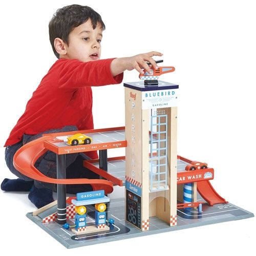 Een jongen in een rood shirt speelt met de Tender Leaf Toys houten garage en servicestation, waarbij hij de helikopter vasthoudt.