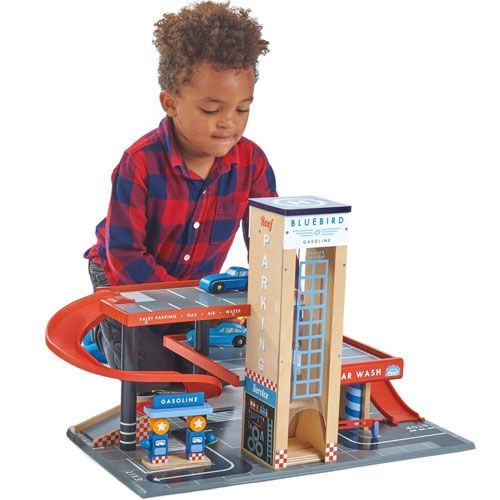 Een jongen in een geruit overhemd speelt met de Tender Leaf Toys houten garage en servicestation.
