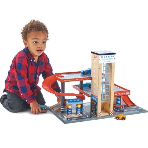 Een jongen in een geruit overhemd speelt op de grond met de Tender Leaf Toys houten garage en servicestation.
