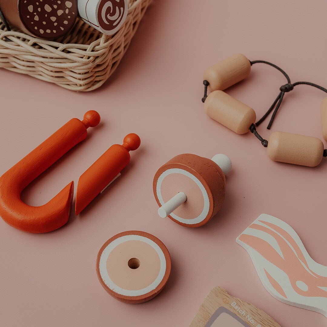 Detail van Tender Leaf Toys houten speelgoed charcuterie, met een worst, ham en spek op een roze ondergrond.