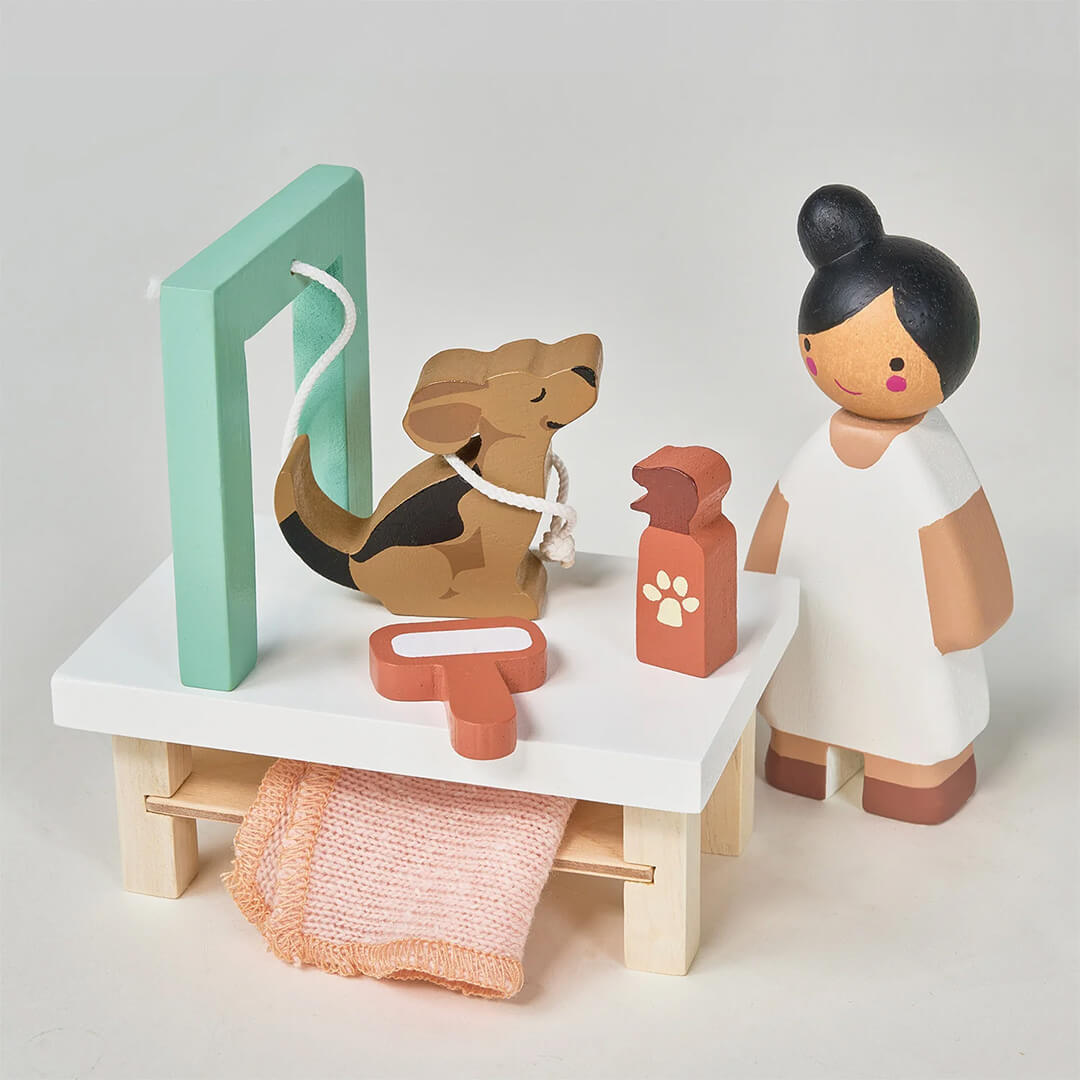 Detailopname van de Tender Leaf Toys houten hondentrimsalon speelset met een trimster, een bruin hondje, een borstel en een flesje shampoo op een trimtafel.