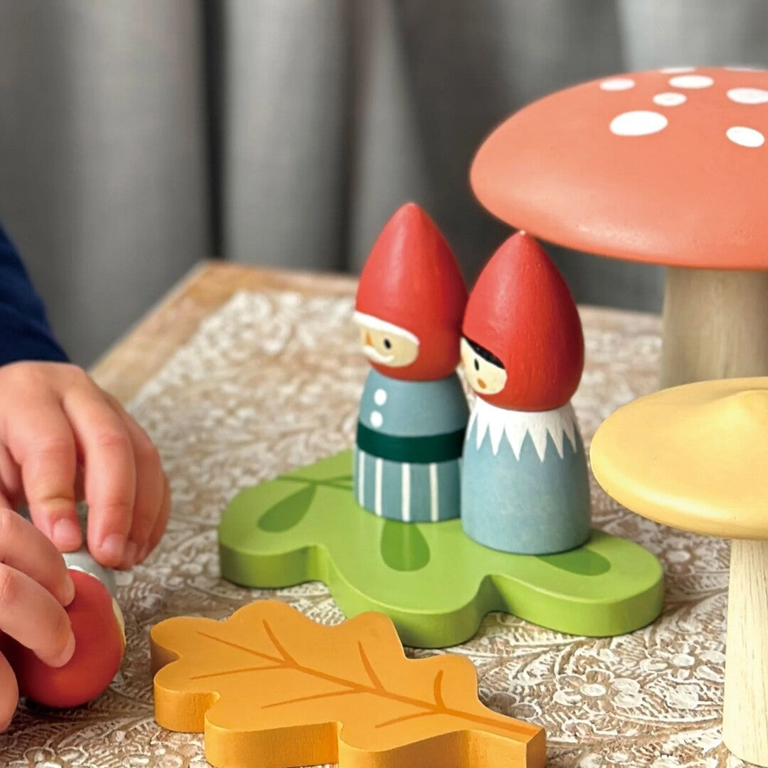 Kinderhanden spelen met twee houten kabouterfiguren op een groene bladbasis.