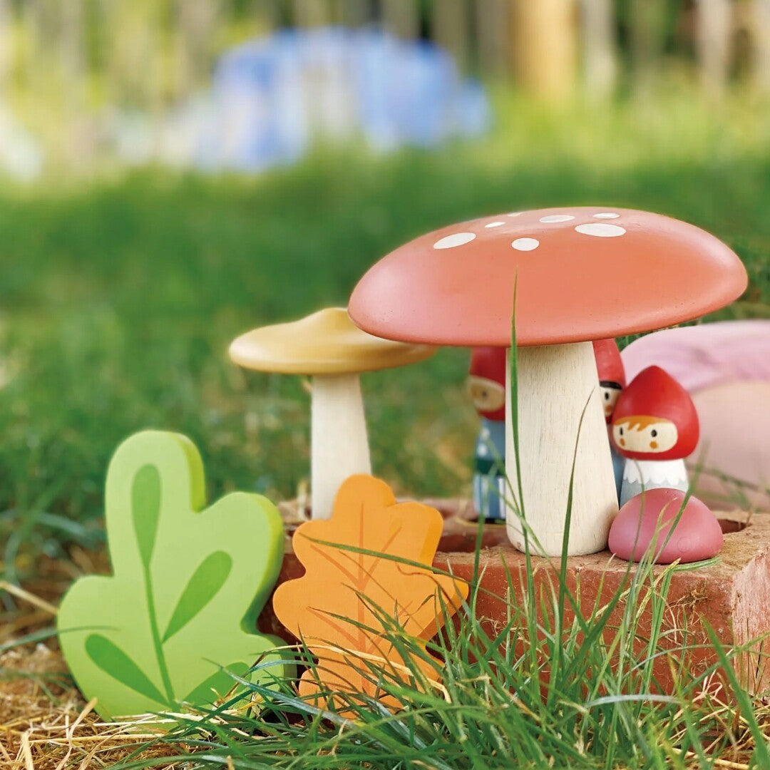 De houten kabouterfamilie speelset met paddenstoelen en bladeren in het gras.