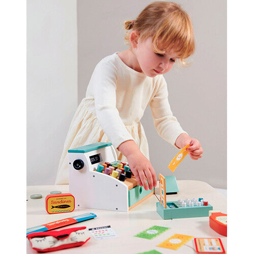 Een kind speelt met de Tender Leaf Toys houten speelgoedkassa en houdt een stuk speelgeld vast.