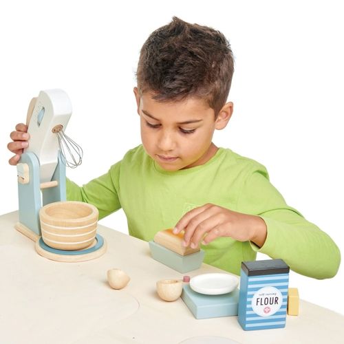 Een kind speelt met de Tender Leaf Toys houten keukenmachine bakset en houdt een broodje vast.