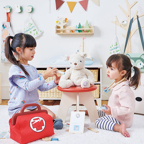 Twee meisjes spelen dokter met een teddybeer op de Tender Leaf Toys paddenstoel kinderkruk.