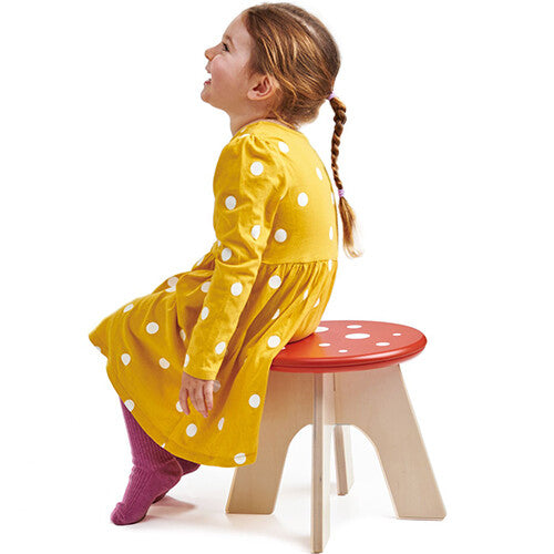 Een lachend meisje zit op de Tender Leaf Toys houten paddenstoel kinderkruk.