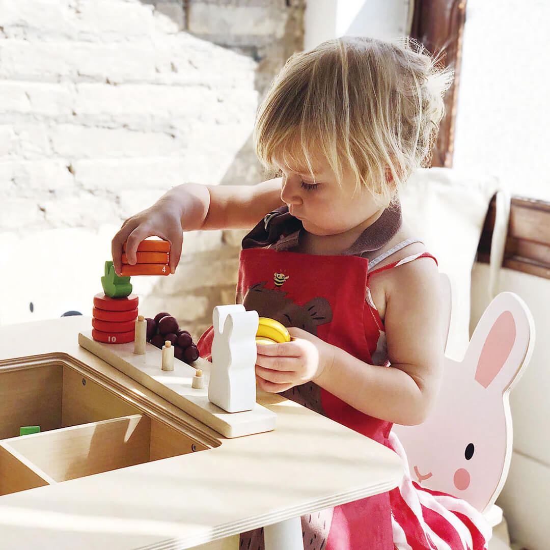 Een peuter speelt met houten speelgoed aan de Tender Leaf Toys kindertafel met konijnenstoel.