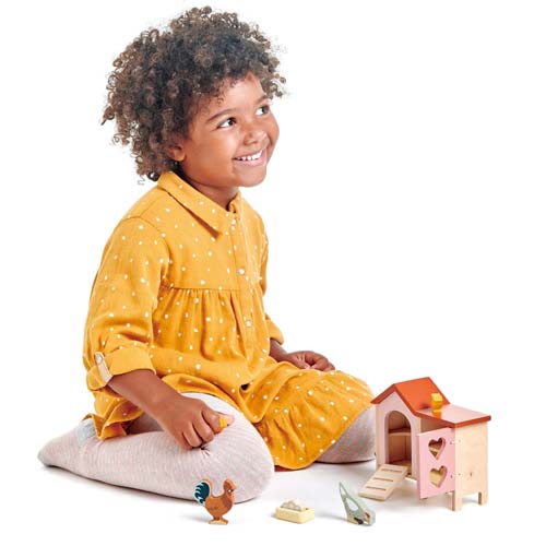 Een lachend meisje speelt op de grond met de Tender Leaf Toys houten kippenhok speelset.