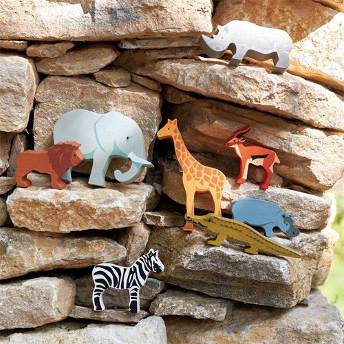 Collectie houten safari dierenfiguren, waaronder een leeuw, olifant en giraffe, op een stenen muur.