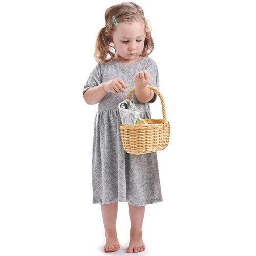 Een kind staat en draagt het Tender Leaf Toys speelgoed boodschappenmandje gevuld met speelgoed.