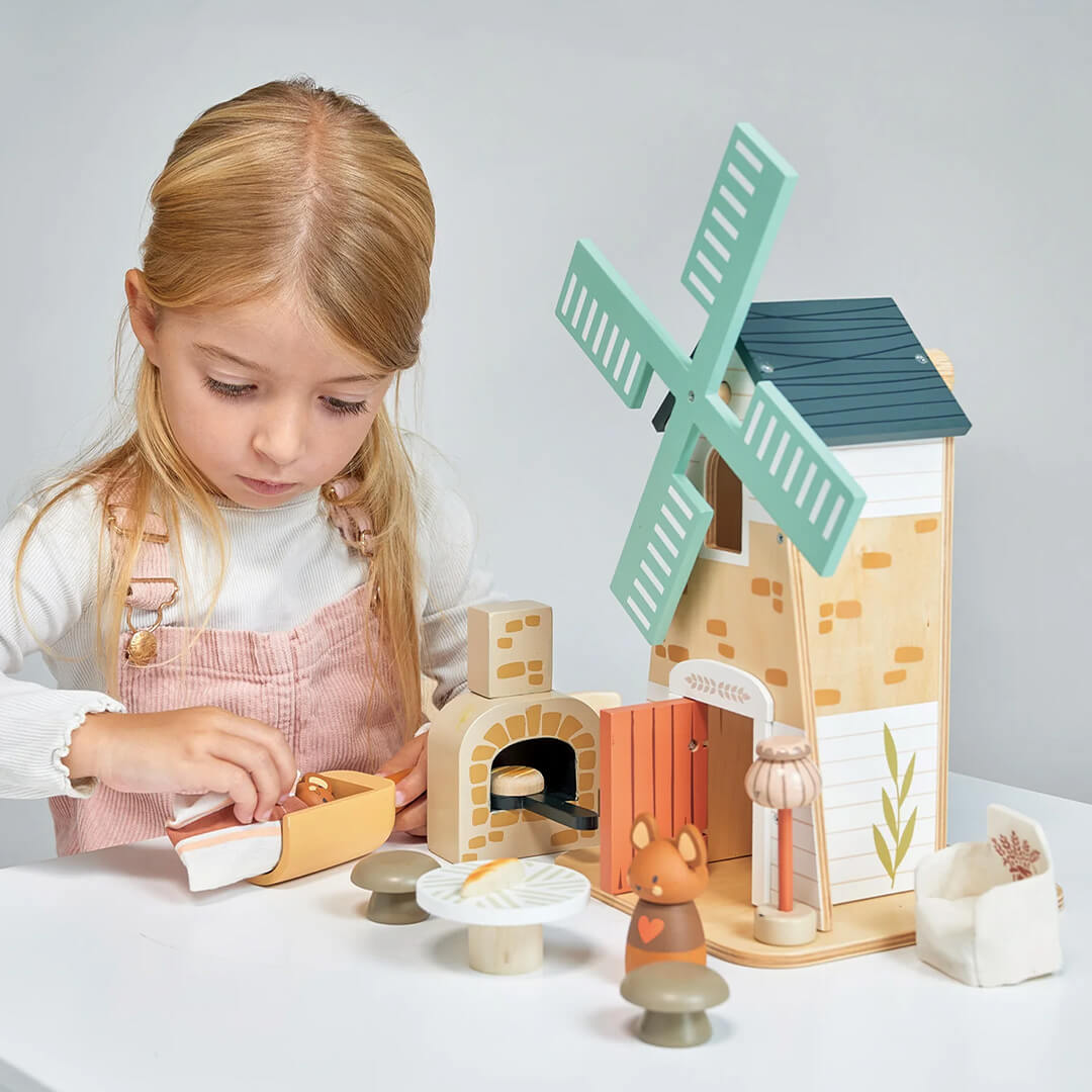 Een meisje speelt met de Tender Leaf Toys houten molen speelset met muizenfiguren en bakkerijaccessoires.