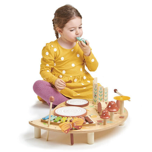 Een meisje blaast op de fluit van de Tender Leaf Toys houten muziekspeelgoedtafel met bosdieren.