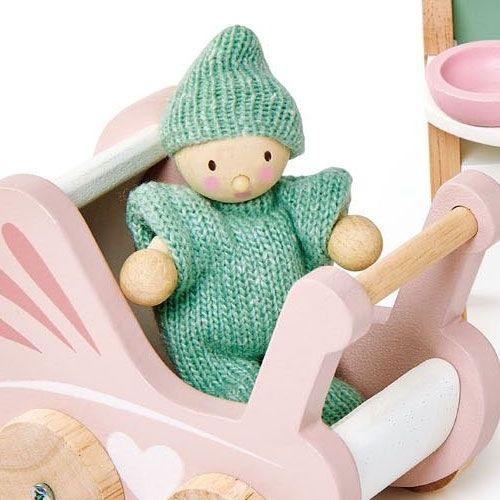 Detail van de Tender Leaf Toys poppenhuis babykamer met een popje in een groen gebreid pakje in de roze houten kinderwagen.