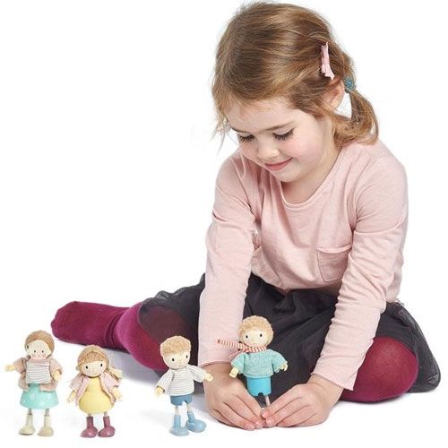 Een meisje speelt met een set Tender Leaf Toys poppenhuispoppen, een houten hond en een skateboard.