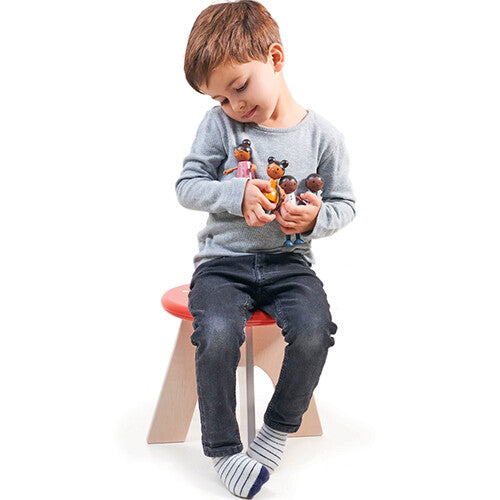 Een jongen zit op een rood krukje en speelt met de Tender Leaf Toys poppenhuispoppen.