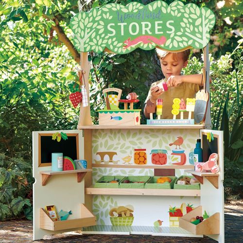 Een jongen speelt met het Tender Leaf Toys houten winkeltje, waar hij speelgoedijsjes en fruit verkoopt.