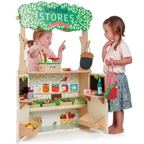 Twee meisjes spelen met het Tender Leaf Toys houten winkeltje, waarbij één achter de toonbank staat met een weegschaal.