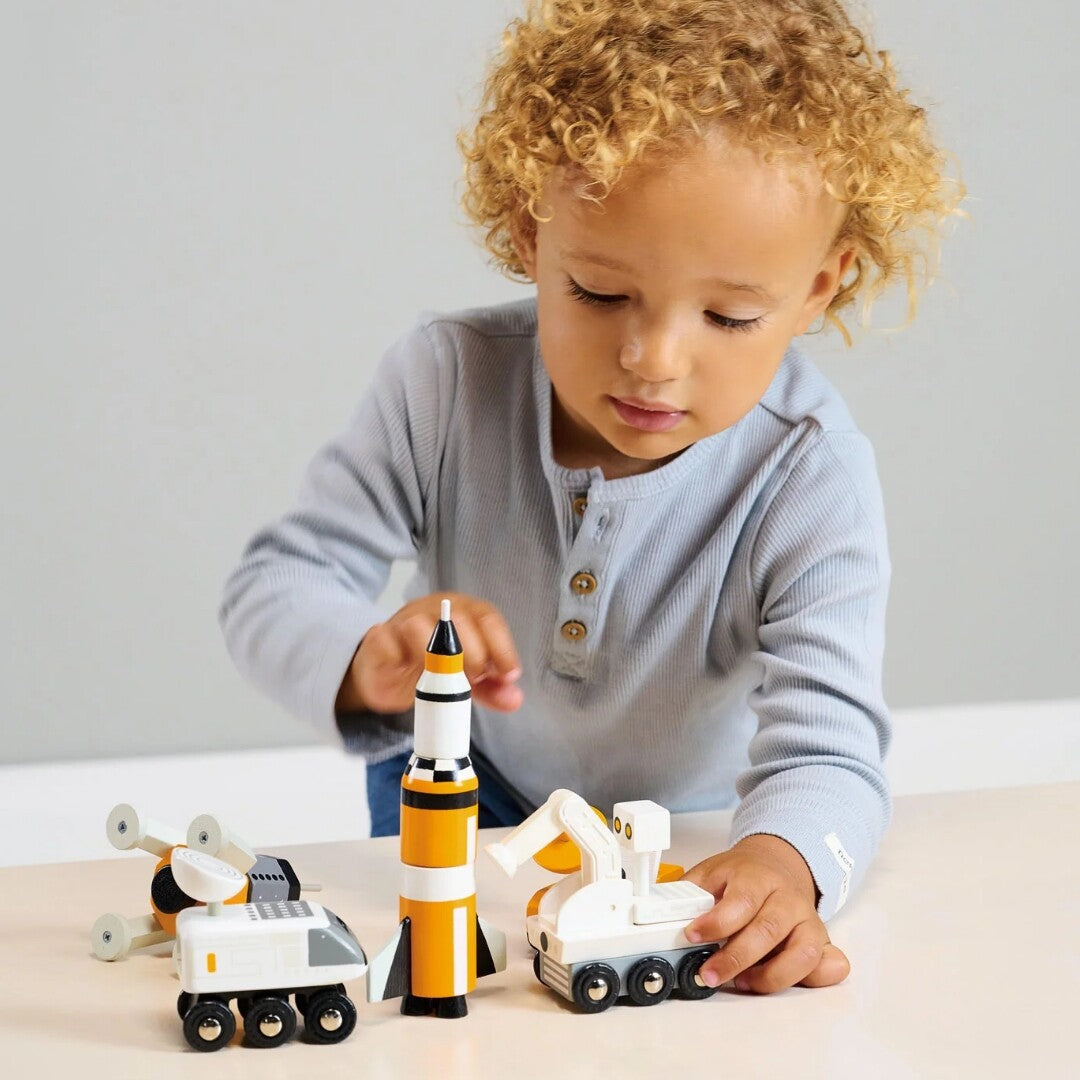 Een kind met blond krullend haar speelt aan tafel met de Tender Leaf Toys houten ruimtevoertuigen.