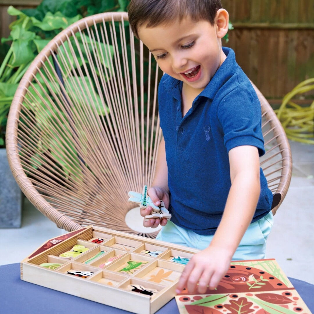 Een lachende jongen speelt met de Tender Leaf Toys houten insectenpuzzel 'Bug Hotel' en houdt een libellestuk vast.