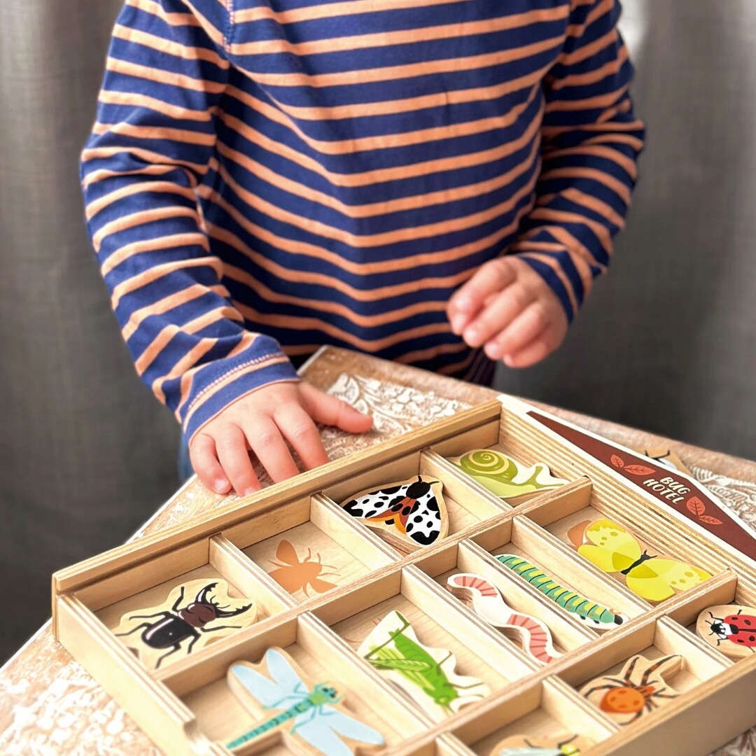 Kinderhanden plaatsen een insectenstuk in de Tender Leaf Toys houten insectenpuzzel 'Bug Hotel'.