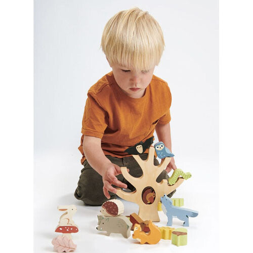 Een kind speelt met het Tender Leaf Toys houten stapelspeelgoed van een herfstbos, waarbij het een uil op de boom plaatst.