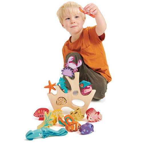 Een jong kind speelt met het Tender Leaf Toys houten stapelspeelgoed met zeedieren en koraal, en houdt een visje vast.