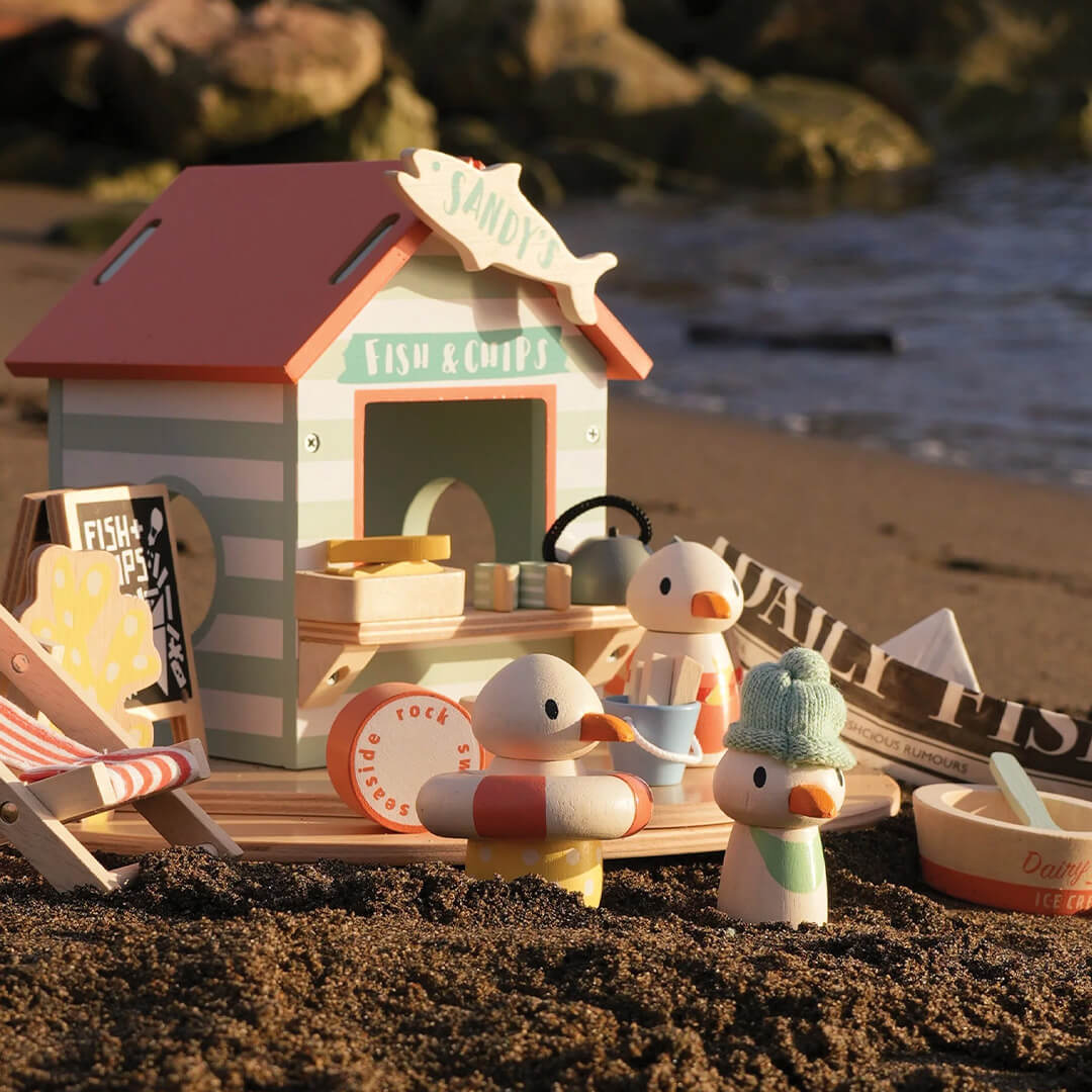 De Tender Leaf Toys speelset strandpaviljoen staat op een zandstrand met de zee op de achtergrond.