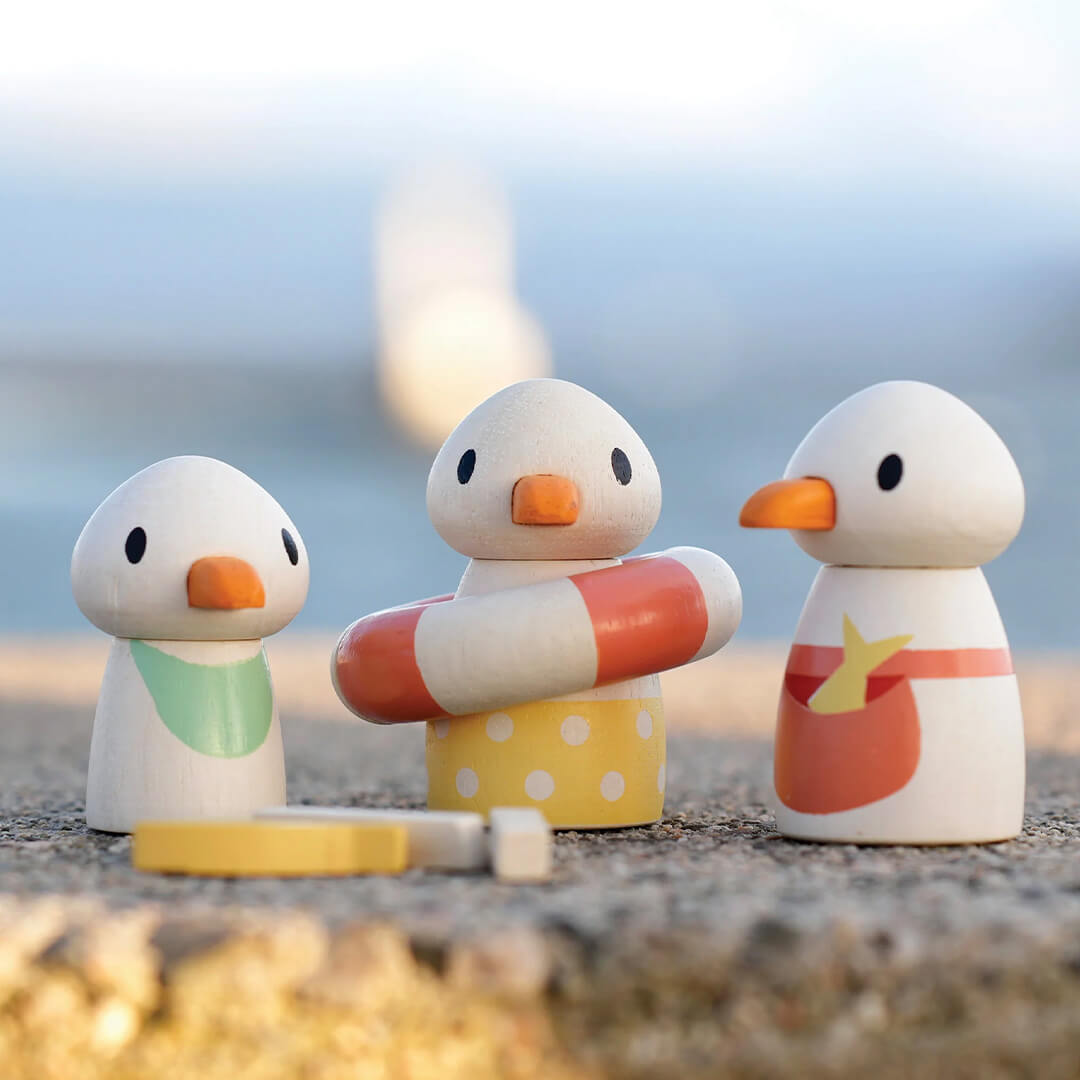 Drie houten eendjes speelfiguren van de strandpaviljoen speelset staan op een stenen ondergrond.