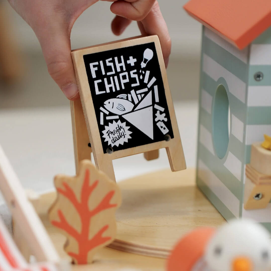 Een hand plaatst een klein houten 'Fish & Chips' uithangbordje bij de speelset.
