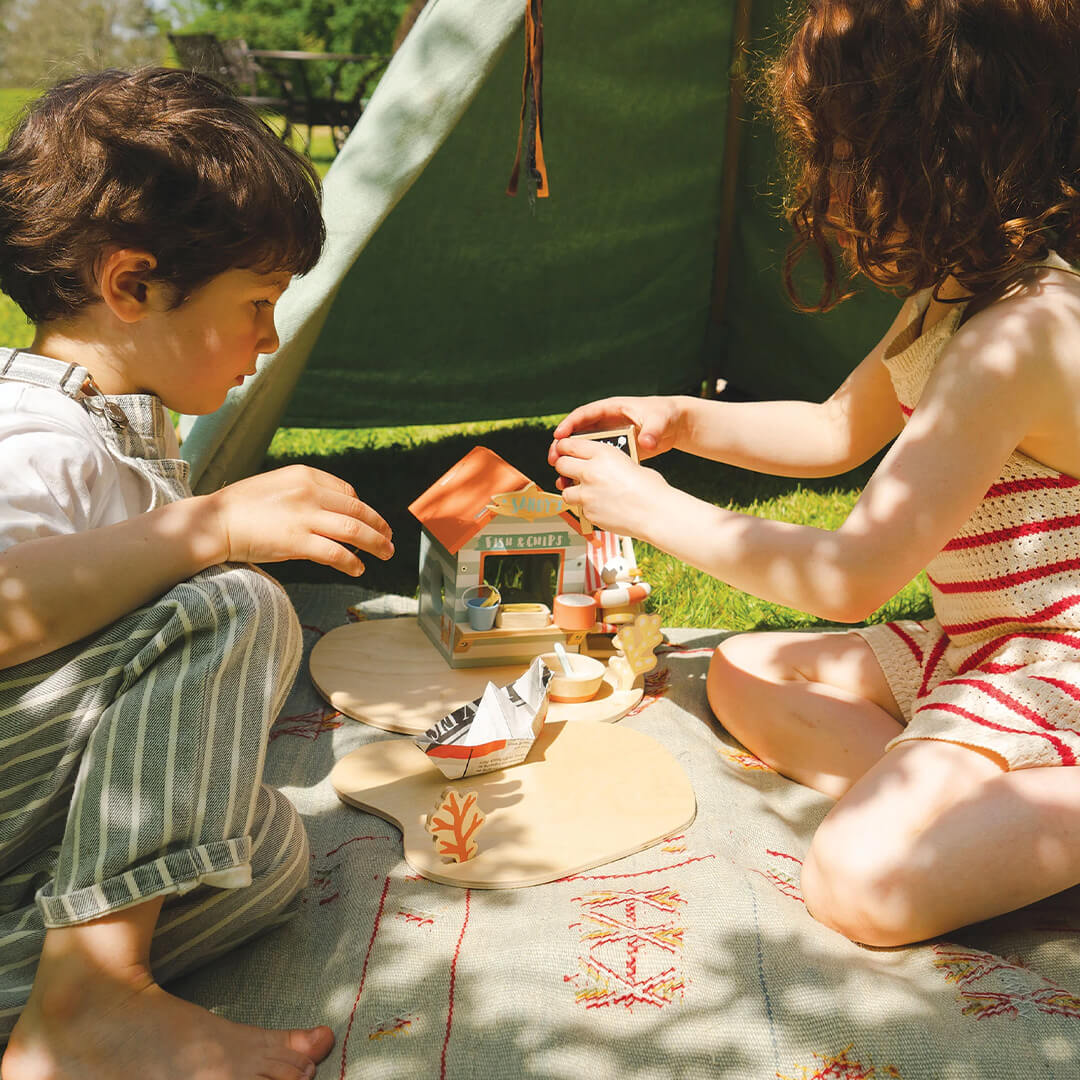 Twee kinderen spelen buiten met de Tender Leaf Toys speelset strandpaviljoen op een deken.