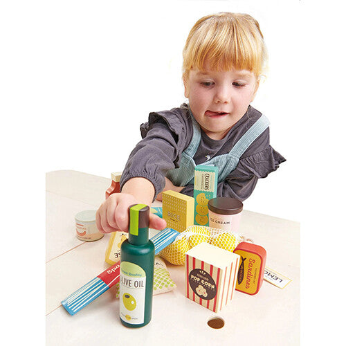 Een kind speelt met de Tender Leaf Toys houten speelgoedboodschappen en pakt een fles olijfolie van tafel.
