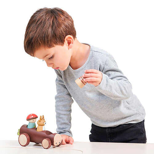 Een kind speelt met de Tender Leaf Toys houten speelgoedauto met bosdierenfiguren op een tafel.