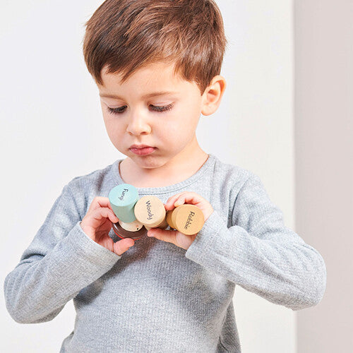 Een kind houdt drie Tender Leaf Toys houten bosdierenfiguren vast.