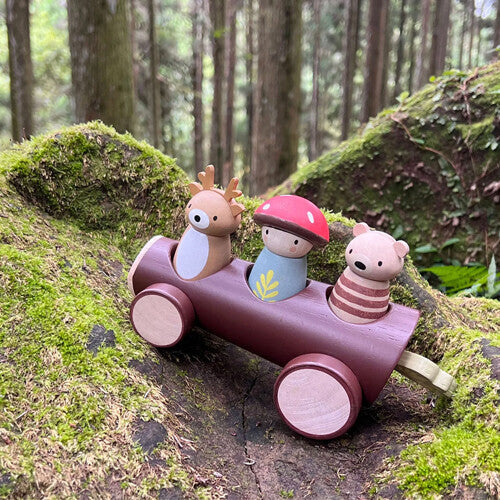 De Tender Leaf Toys houten speelgoedauto met bosdierenfiguren staat op een bemoste boomstam in het bos.