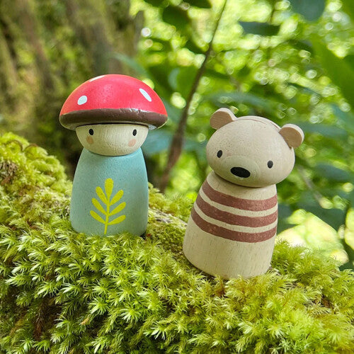 De Tender Leaf Toys houten paddenstoel- en beerfiguren staan op mos in een bosrijke omgeving.