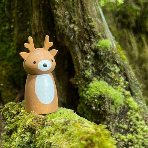 Een detailfoto van het Tender Leaf Toys houten hertfiguur op mos bij een boomstam.