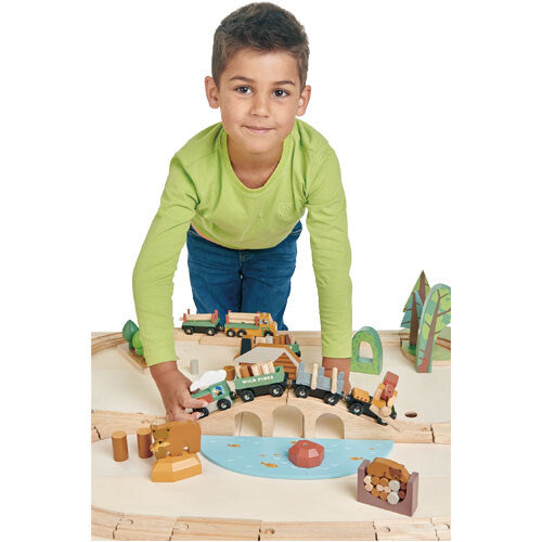 Een jongen speelt met de tender leaf toys houten treinbaan dennenbos, staand achter de tafel.