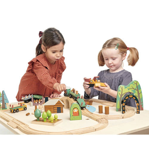 Twee kinderen spelen met de tender leaf toys houten treinbaan dennenbos, waarbij een meisje een kraan vasthoudt.