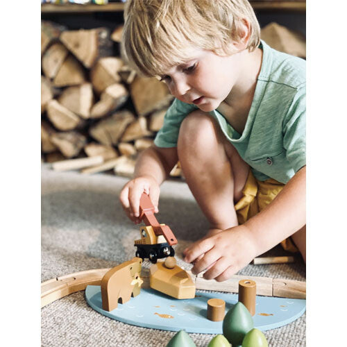 Een jongen speelt met de tender leaf toys houten treinbaan dennenbos, waarbij hij een kraan bedient.