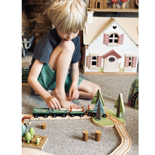 Een jongen speelt met de tender leaf toys houten treinbaan dennenbos, zittend op de grond.