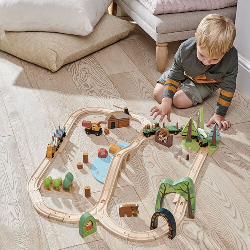Een jongen speelt met de tender leaf toys houten treinbaan dennenbos, die op een houten vloer ligt.