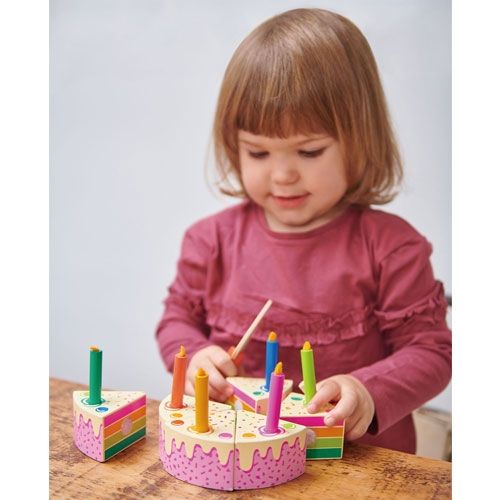 Een kind speelt met de Tender Leaf Toys houten speelgoed verjaardagstaart met regenbooglagen en kaarsjes.