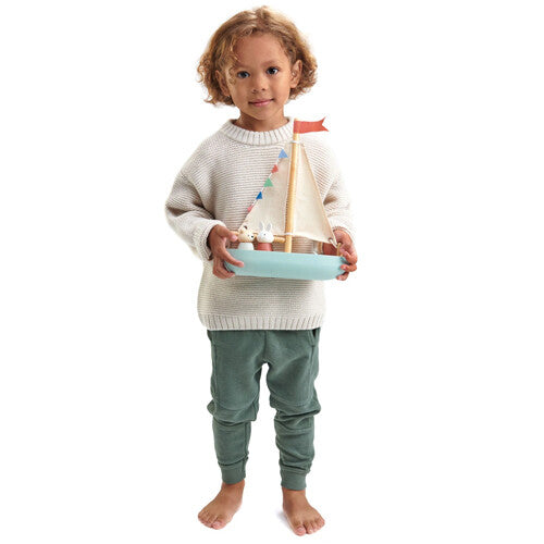 Een kind staat en houdt de Tender Leaf Toys houten speelgoedzeilboot met de dierenfiguren vast.