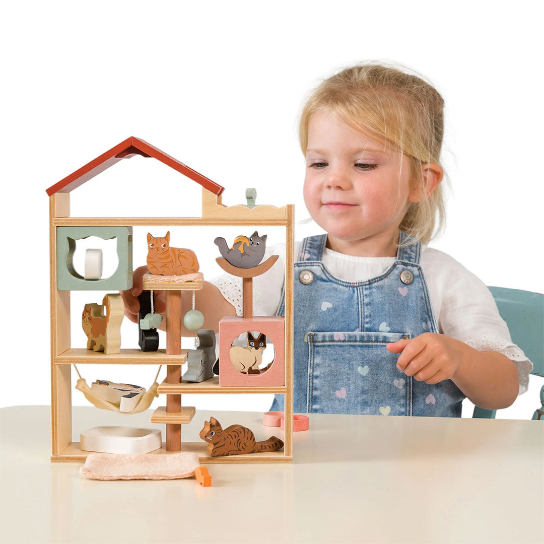 Een jong meisje kijkt glimlachend naar de Tender Leaf Toys houten kattenhotel speelset.