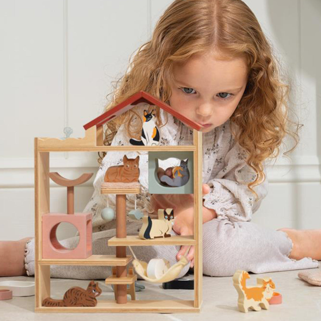 Een meisje met lang haar zit op de grond en kijkt geconcentreerd naar de Tender Leaf Toys houten kattenhotel speelset.