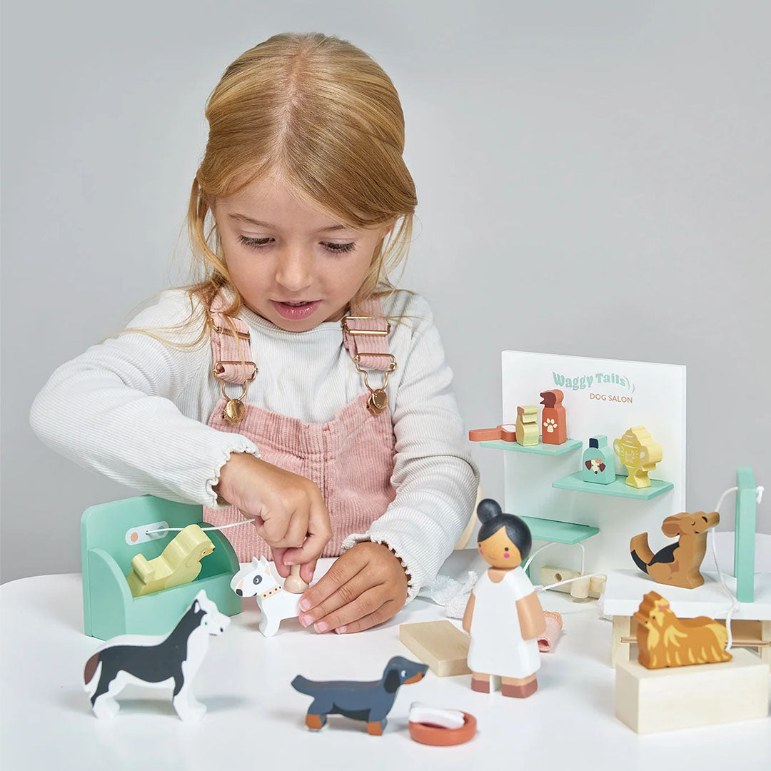Een meisje speelt met de Tender Leaf Toys houten hondentrimsalon speelset, waarbij ze een wit hondje borstelt.