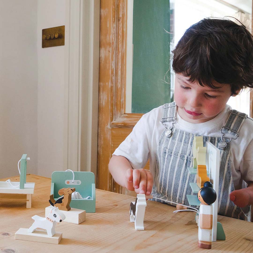 Een jongen speelt met de Tender Leaf Toys houten hondentrimsalon speelset op een houten tafel.