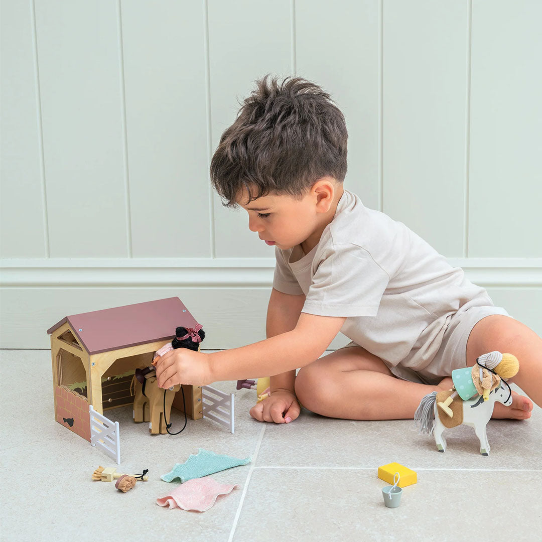 Jongen speelt op de vloer met de Tender Leaf Toys houten paardenstal speelset.